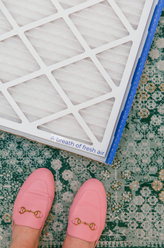 How to Improve Air Quality in Home by popular Houston lifestyle blog, Cake and Confetti: image of a woman wearing pink loafers and standing next to a Homestock USA air filter. 