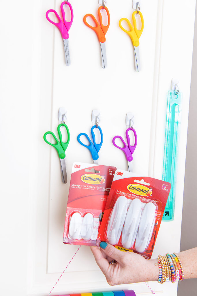Craft Closet by popular Houston lifestyle blog, Cake and Confetti: image of a woman holding Command hooks in front of individual paper scissors hanging on Command hooks mounted to a door. 