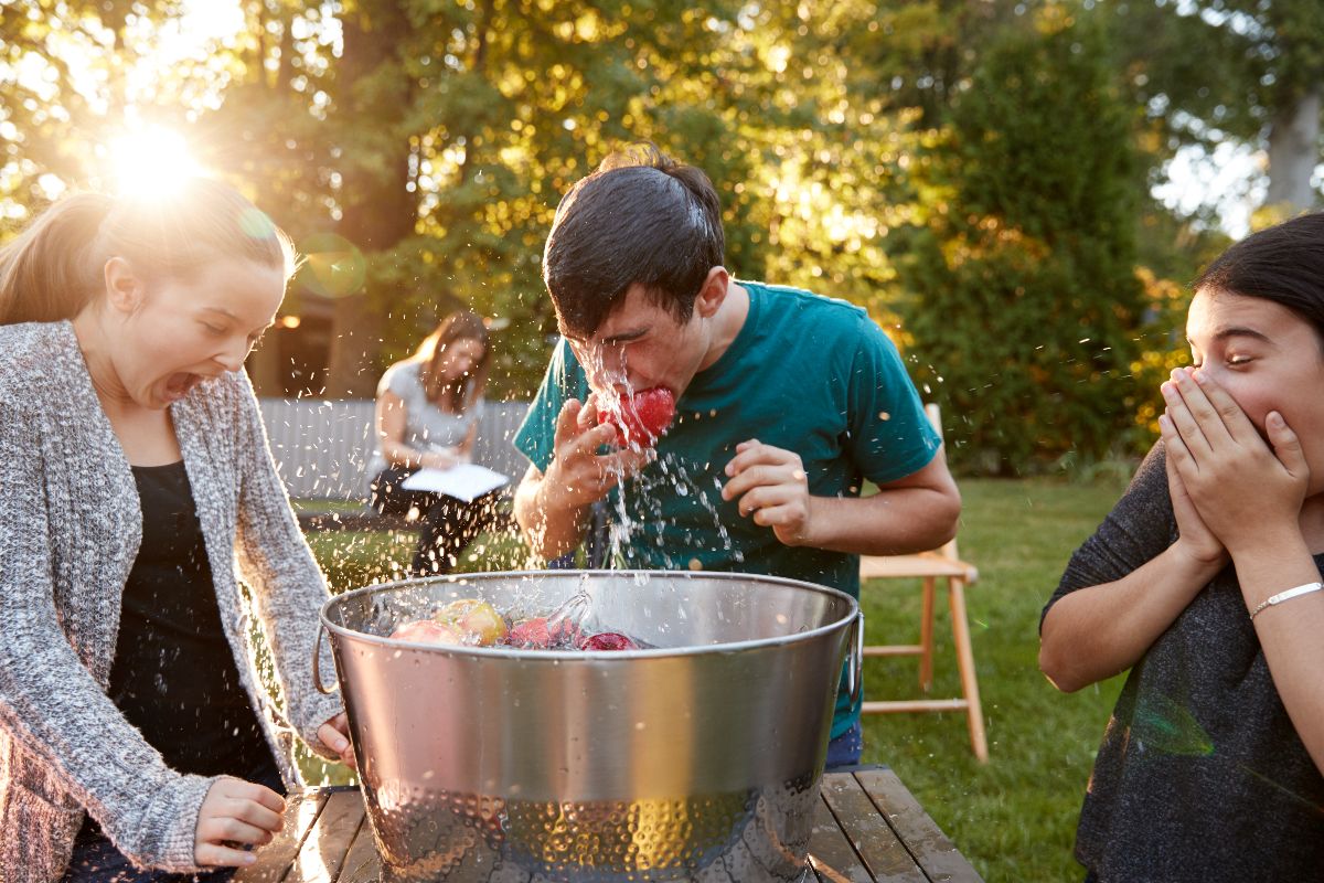 Three friends playing with apple in an aluminum pail full of water